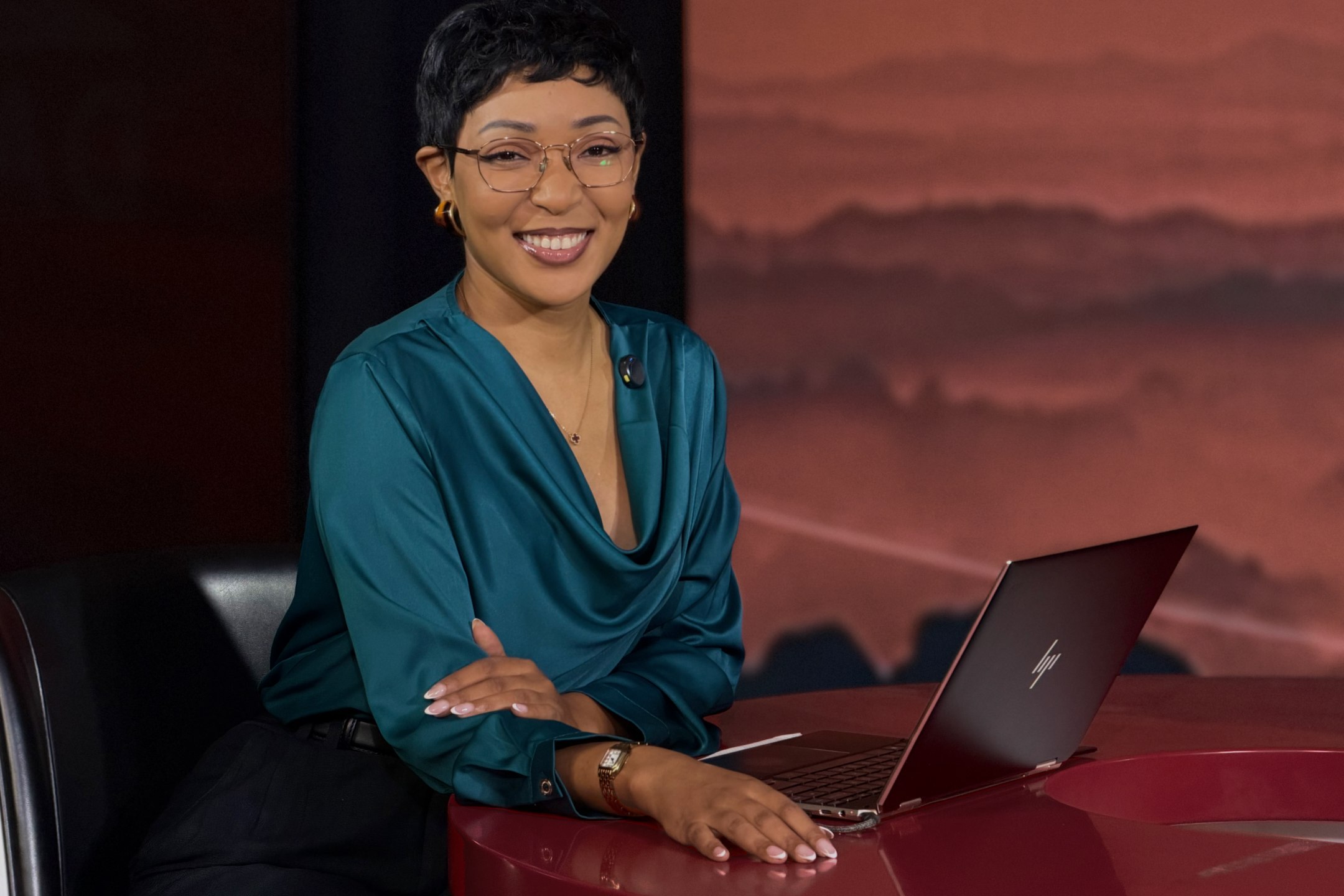 Yolanda Robert seated at a red studio desk with her laptop, in a broadcast studio during production